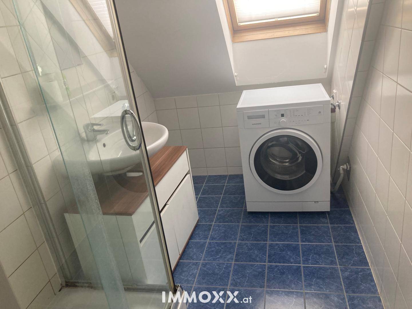 Badezimmer im Dachgeschoss mit Dusche, Waschbecken, Waschmaschine und blauen Fliesen.