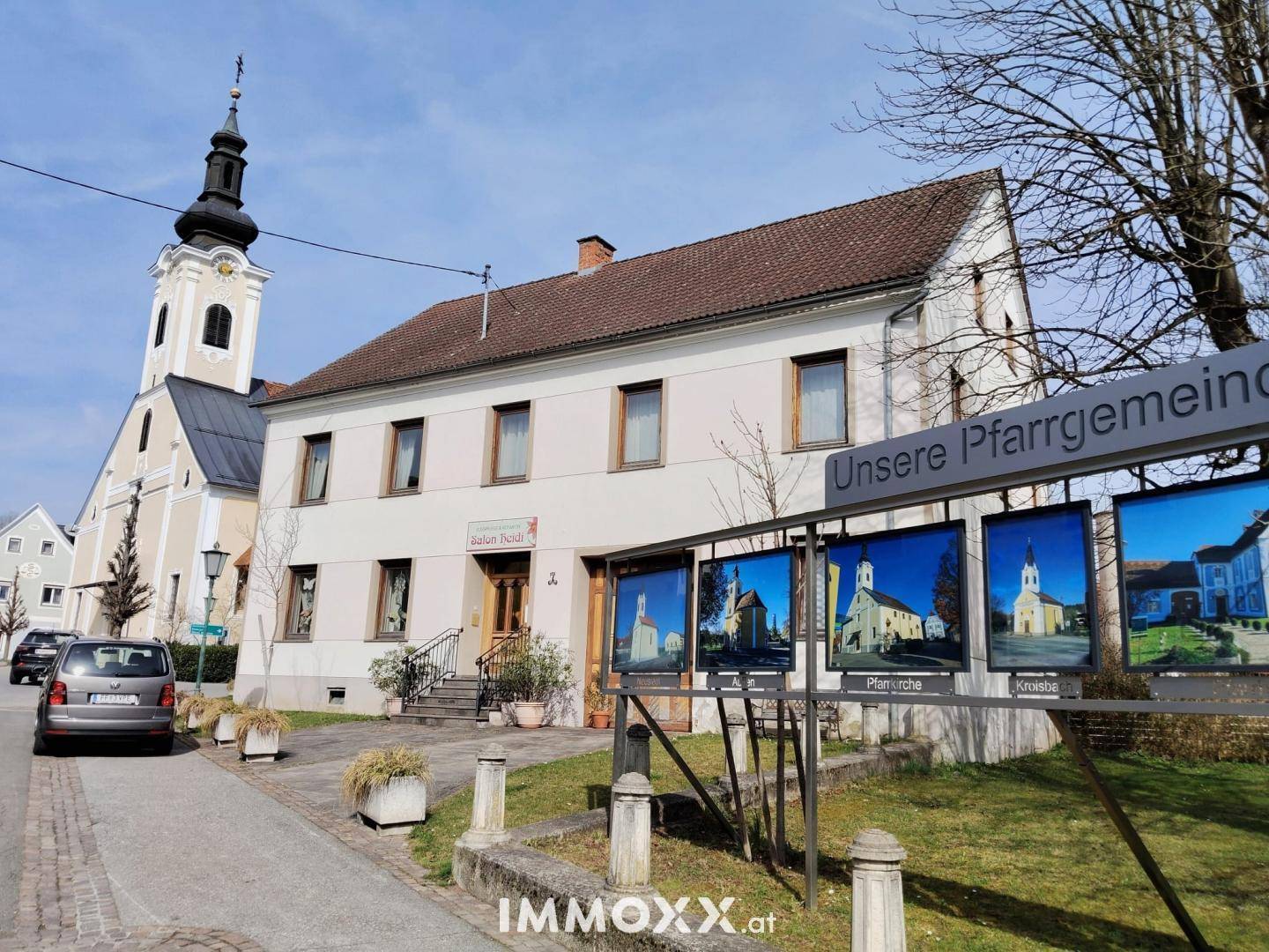 Historisches Gebäude mit Kirche im Hintergrund und einer Informationstafel im Vordergrund.