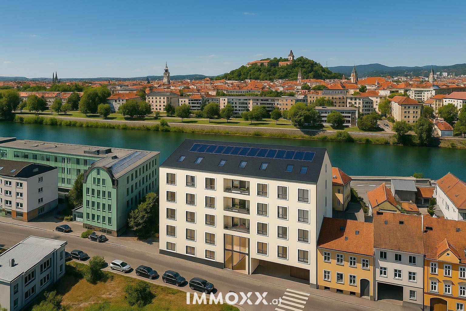 Luftaufnahme eines modernen Wohngebäudes am Flussufer mit Stadt- und Bergblick.