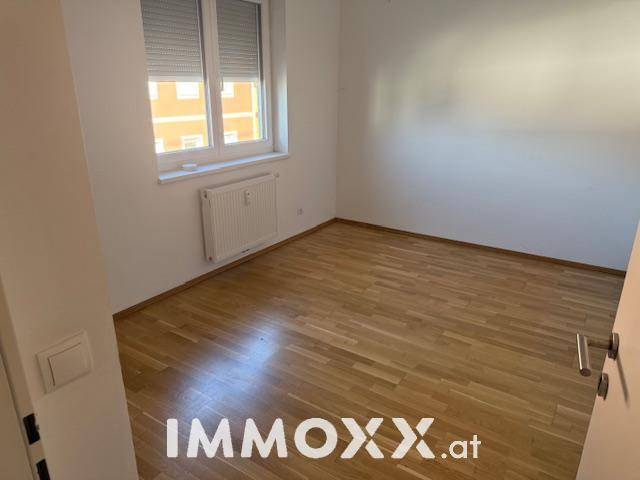 Leeres Zimmer mit hellem Holzparkettboden und einem Fenster mit Rollläden.