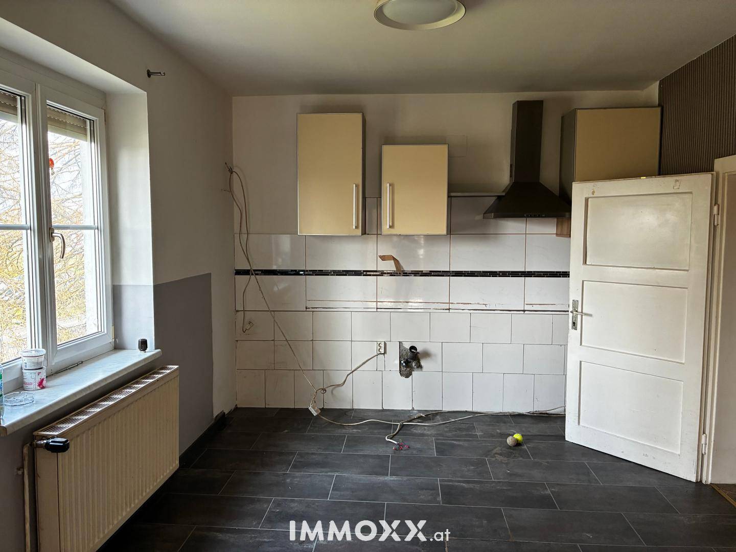 Unfertige Küche mit Fliesenboden, alten Schränken und einem Fenster.