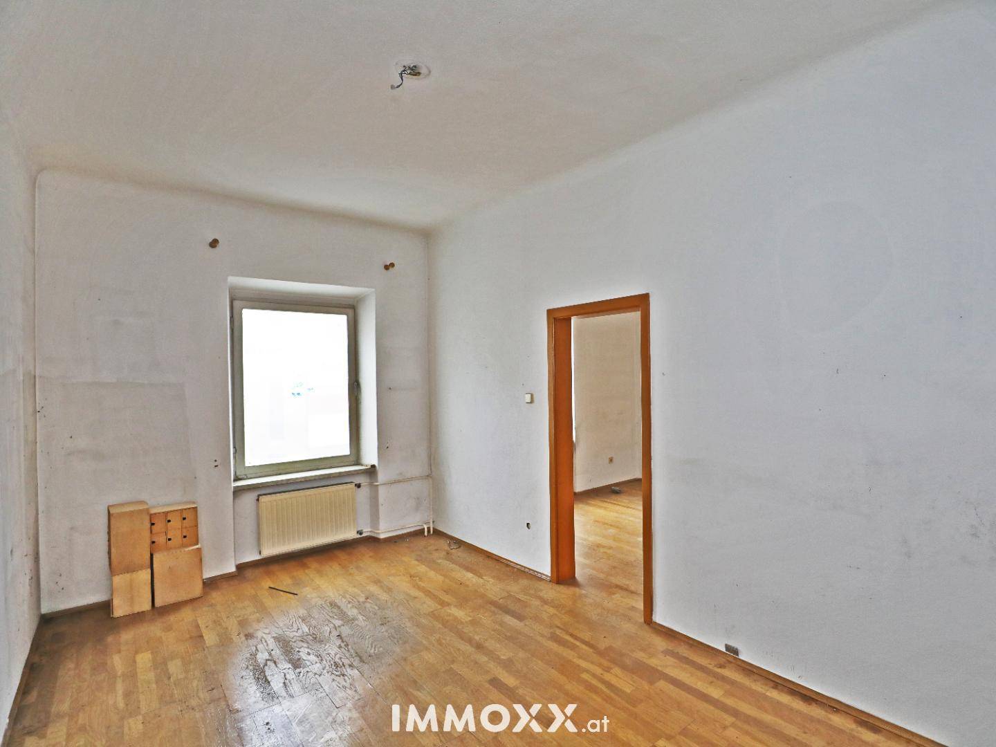 Heller Raum mit Parkettboden und einem Fenster, bietet Potenzial für eine Neugestaltung.