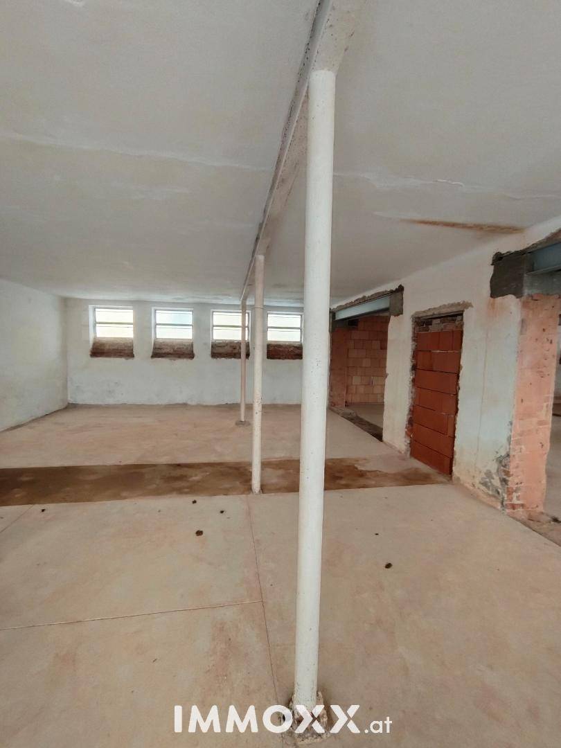 Großer, unfertiger Kellerraum mit Betonboden und kleinen Fenstern.