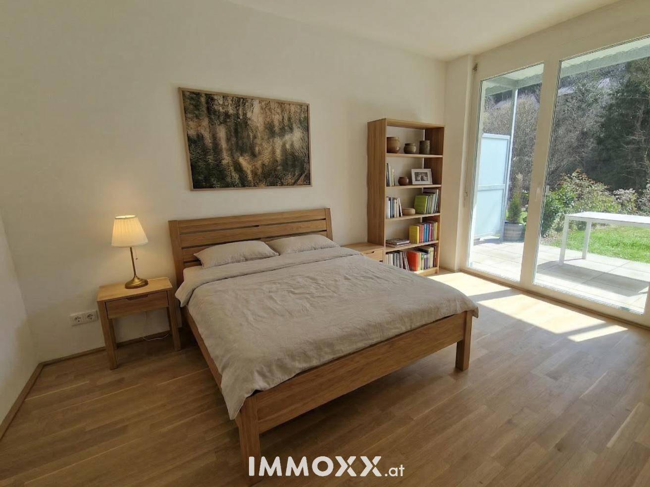 Schlafzimmer mit Holzbett, Parkettboden und großen Fenstern mit Blick ins Grüne.