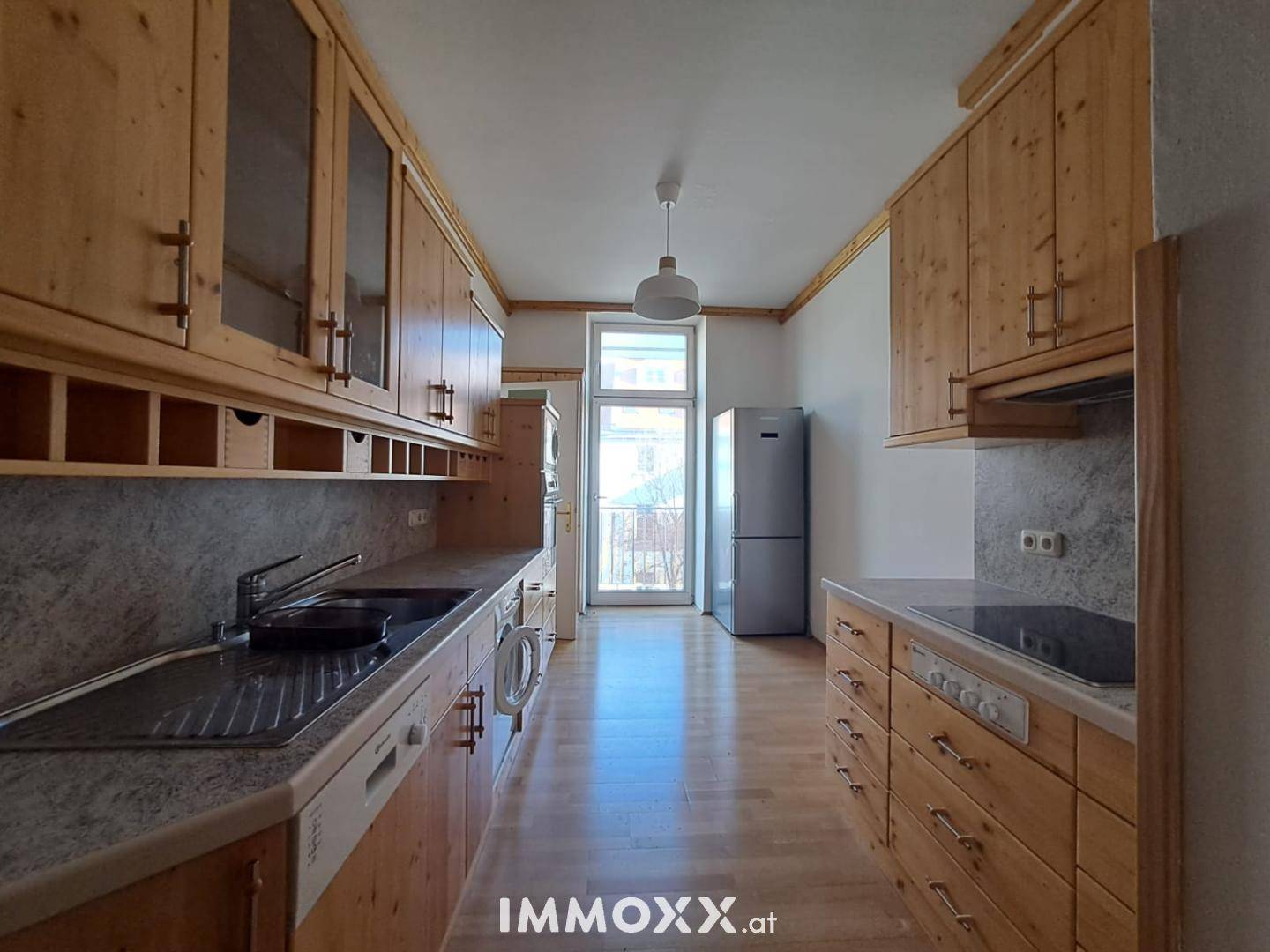 Küche mit Holzschränken, integrierten Geräten und Zugang zu einem kleinen Balkon.