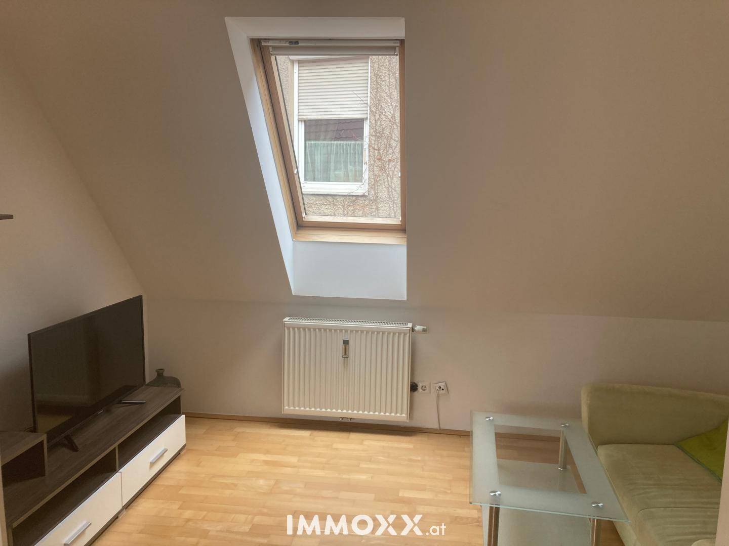 Gemütliches Wohnzimmer im Dachgeschoss mit schrägen Wänden, Dachfenster und Fernseher.