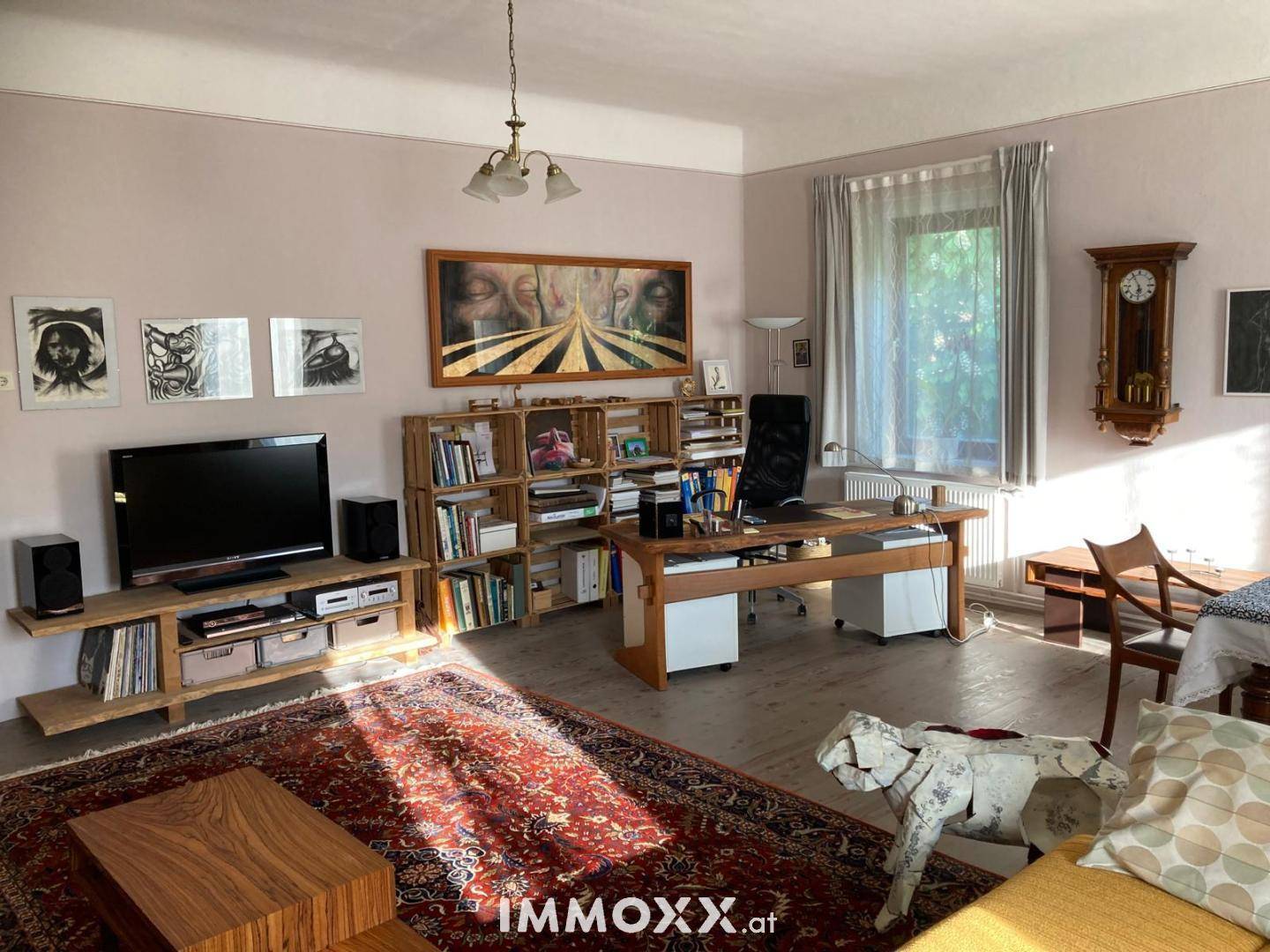 Geräumiges Wohnzimmer mit Schreibtisch, Teppichboden und Blick ins Grüne.