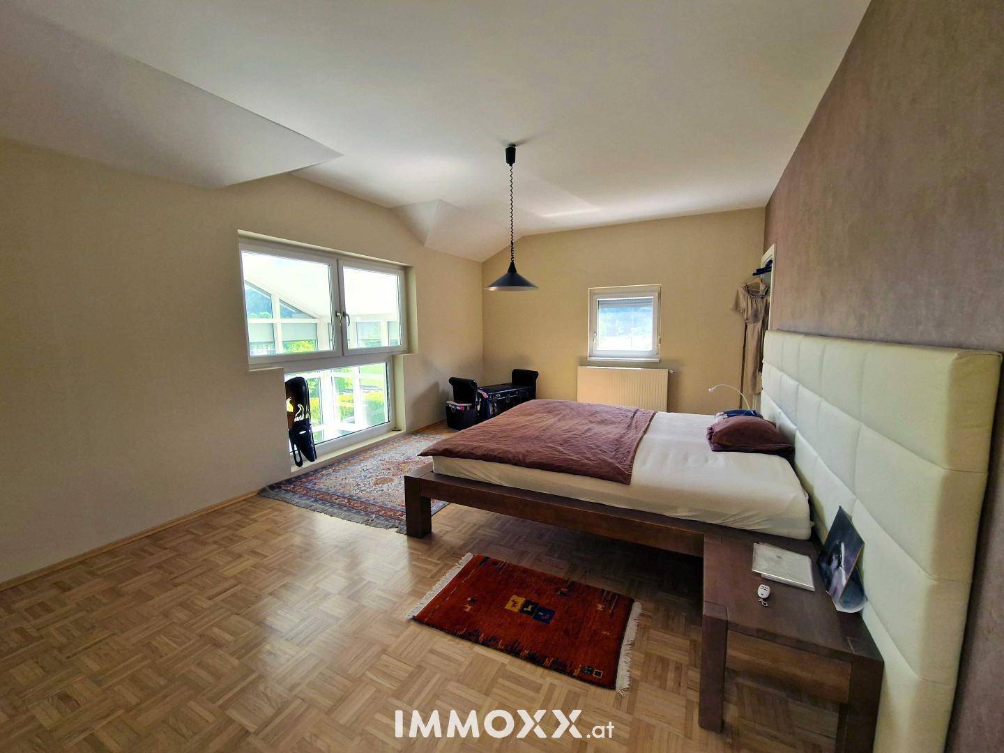 Geräumiges Schlafzimmer mit Doppelbett, Parkettboden und Fenster mit Blick ins Grüne.