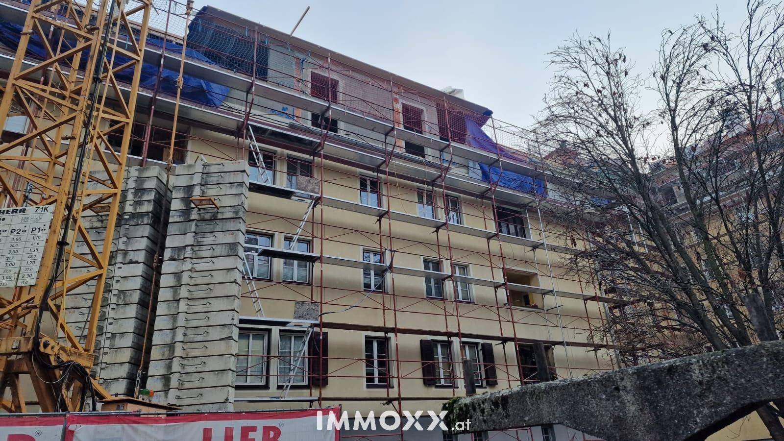 Fassade eines Wohngebäudes mit Gerüst und Baukran während der Renovierungsarbeiten.