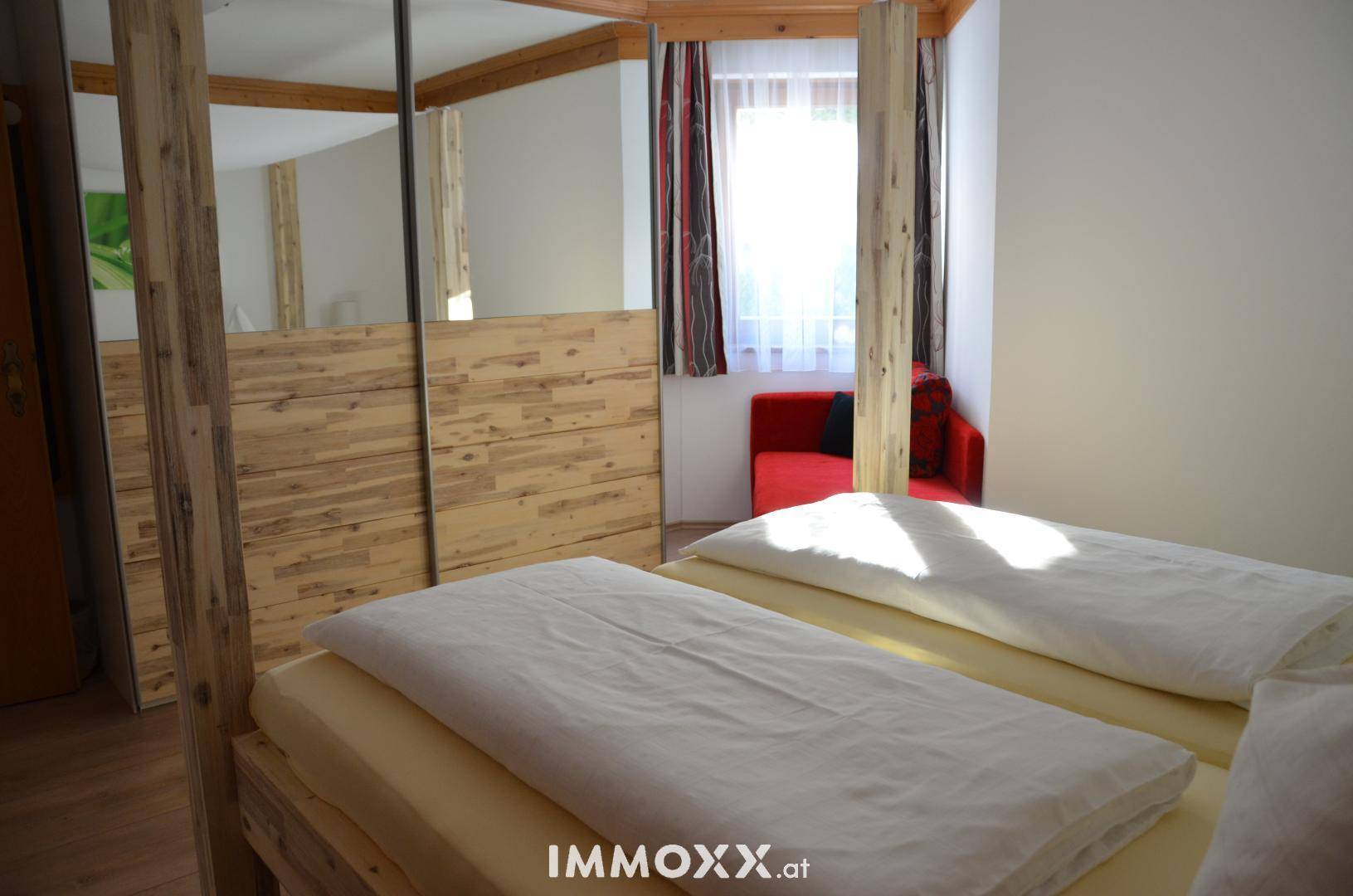 Schlafzimmer mit Himmelbett aus Holz, einem großen Spiegelschrank und Blick auf ein Fenster.