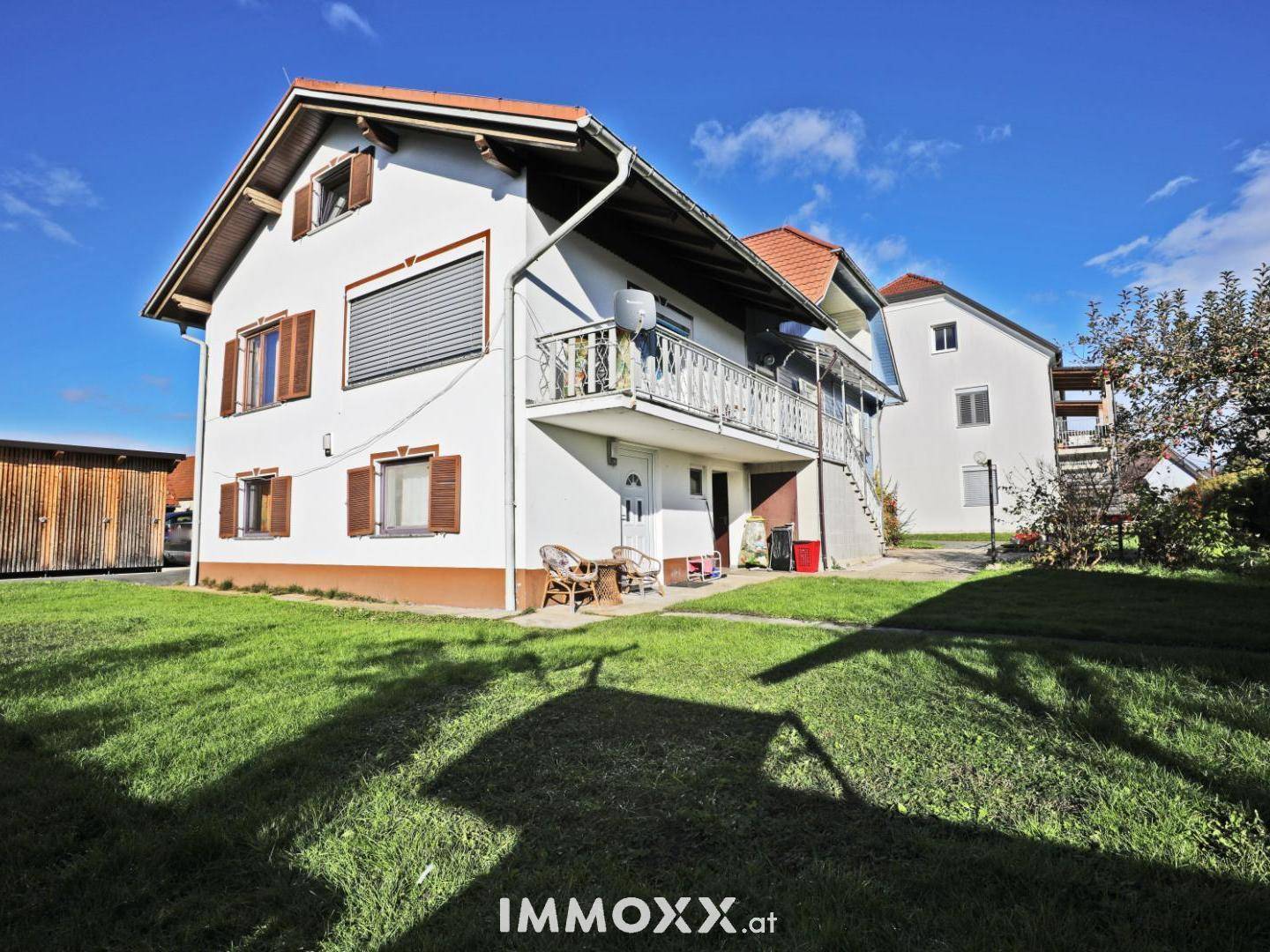 Rückseite des Hauses mit Balkon, kleiner Terrasse und weitläufigem Rasenbereich.