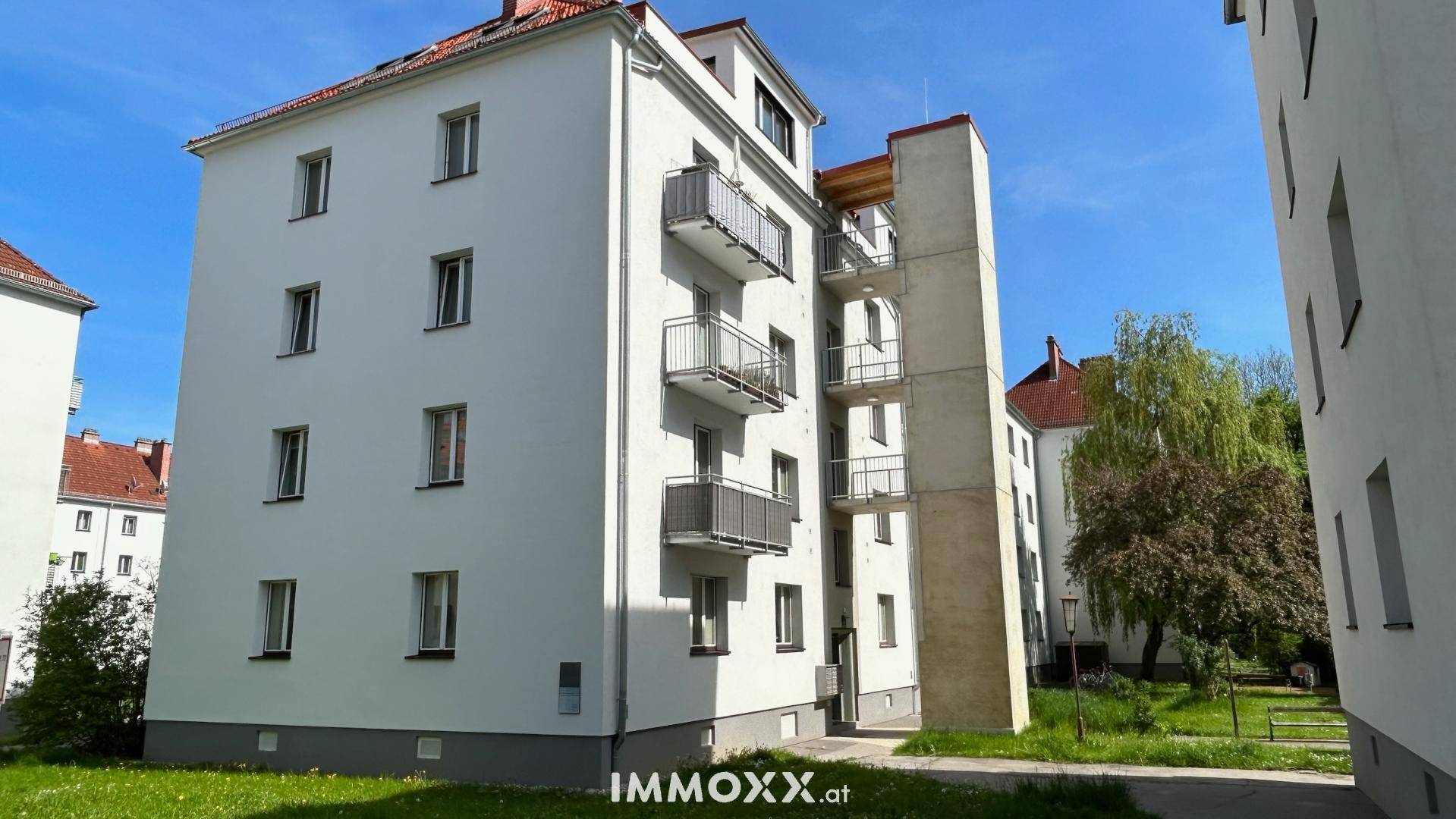 Modernisiertes Mehrfamilienhaus mit weißer Fassade, Balkonen und externem Aufzug.