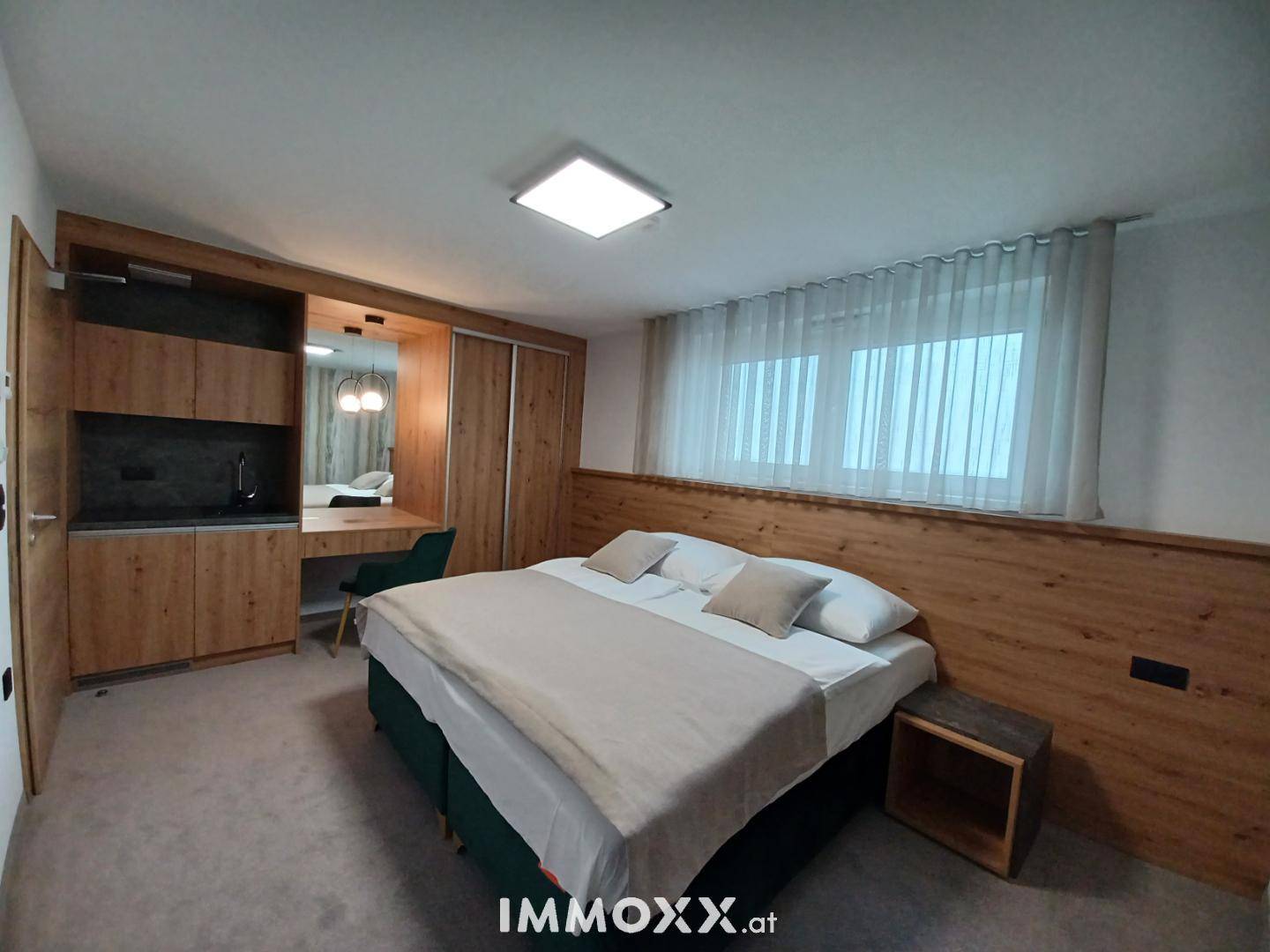 Helles Schlafzimmer mit Doppelbett, Holzvertäfelung und Fenster mit Vorhängen.