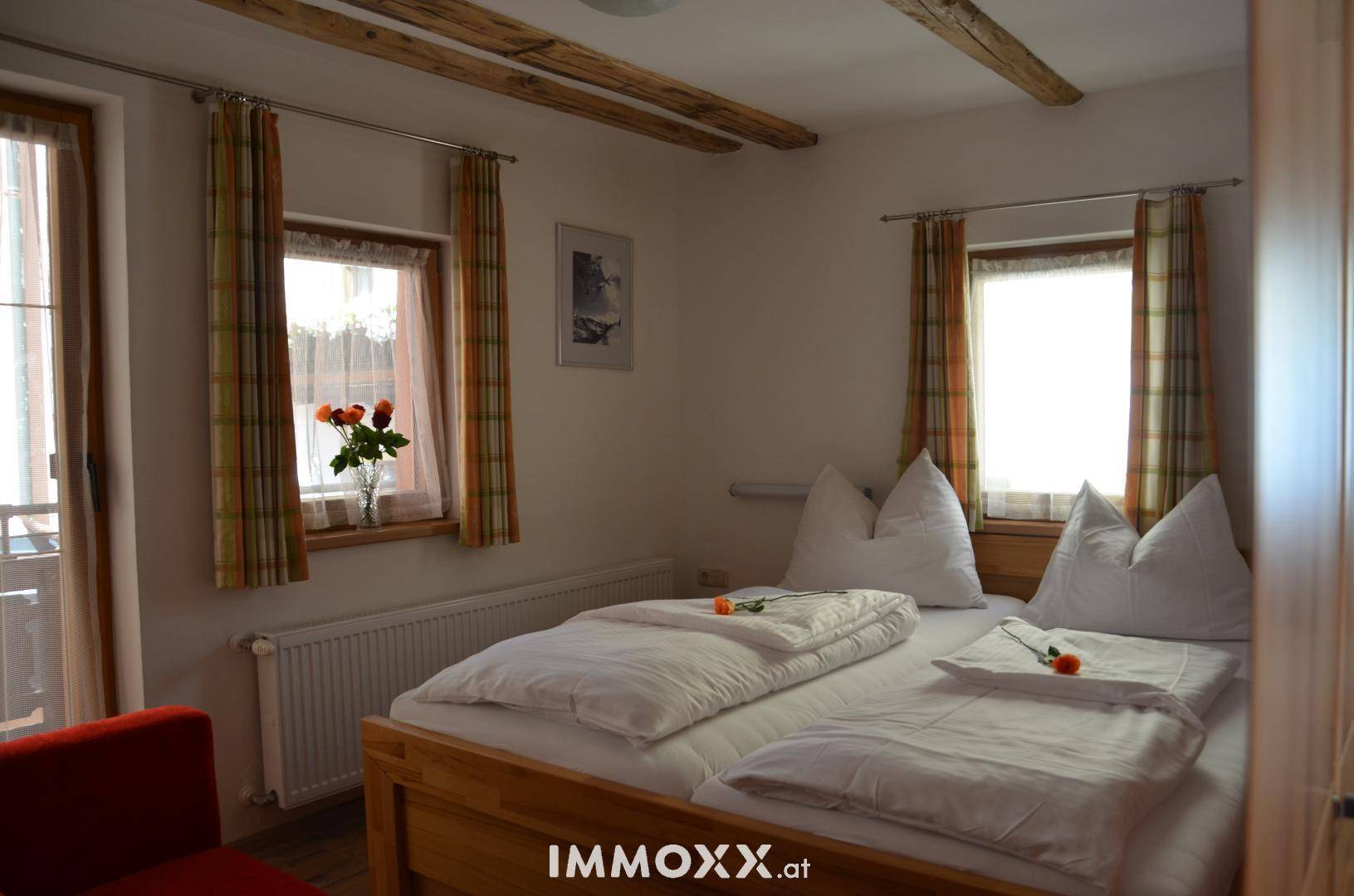 Helles Schlafzimmer mit zwei Betten, Holzbalken an der Decke und Zugang zu einem Balkon durch eine Tür.
