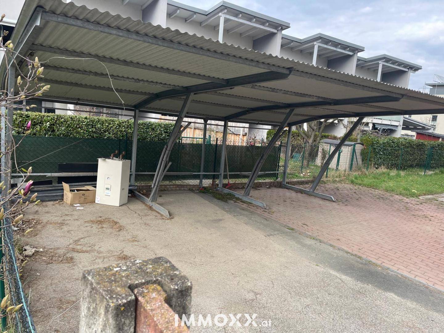 Überdachter Carport mit Wellblechdach und Metallkonstruktion für mehrere Fahrzeuge im Freien.