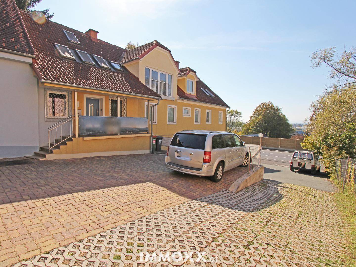 Außenansicht des Gebäudes mit gepflasterter Auffahrt, Parkplätzen und einem geparkten Van.