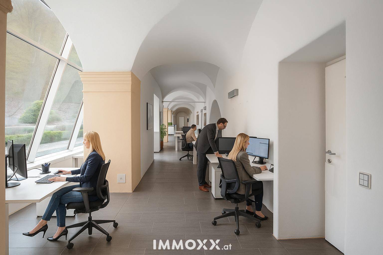 Großzügliches Großraumbüro mit gewölbten Decken und großen, schrägen Fenstern, mehrere Mitarbeiter arbeiten.