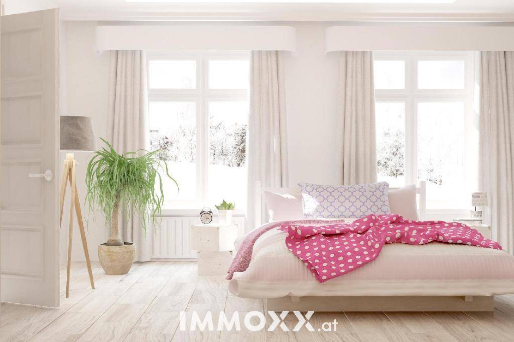 Helles Schlafzimmer mit weißem Holzboden, großen Fenstern und einem bequemen Bett mit rosa Decke.