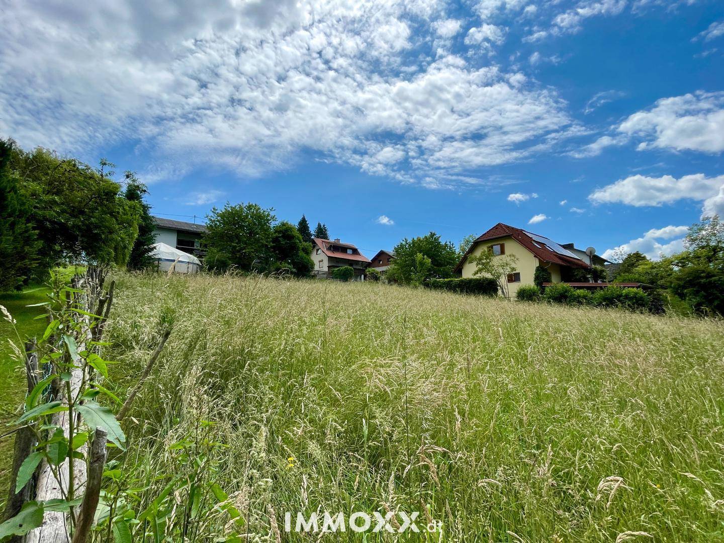 Weitläufiges Wiesengrundstück mit Blick auf ein Wohnhaus und umgebende Natur unter blauem Himmel.