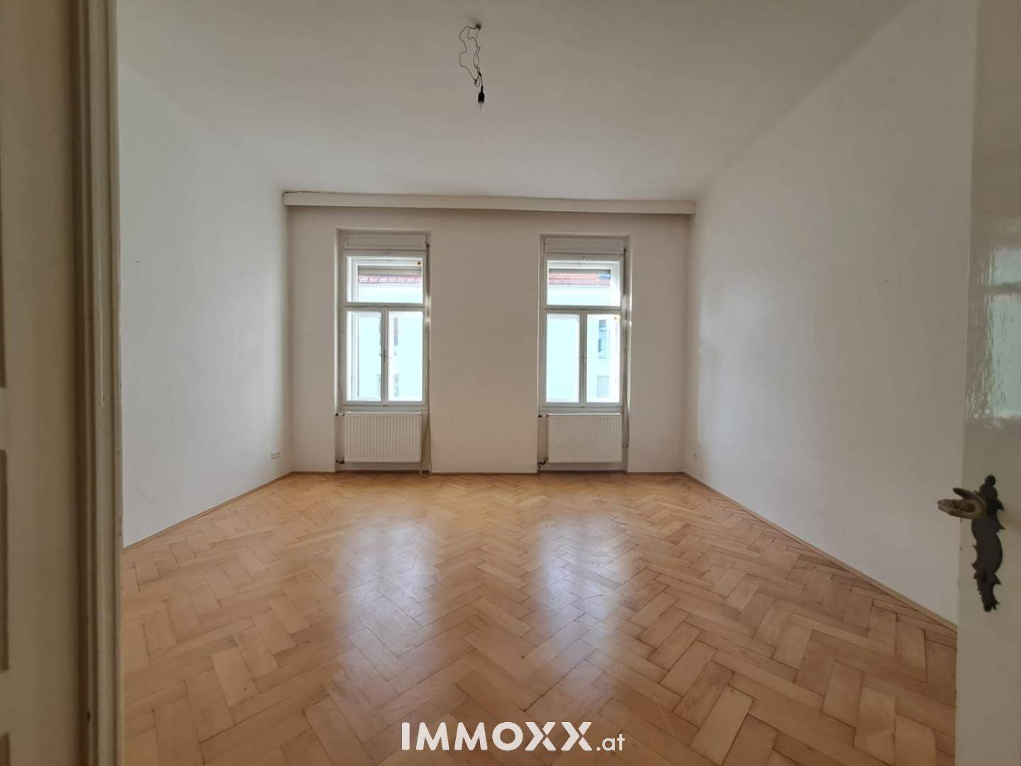 Heller Raum mit Fischgrätparkettboden und zwei großen Fenstern, ideal als Wohn- oder Schlafzimmer.