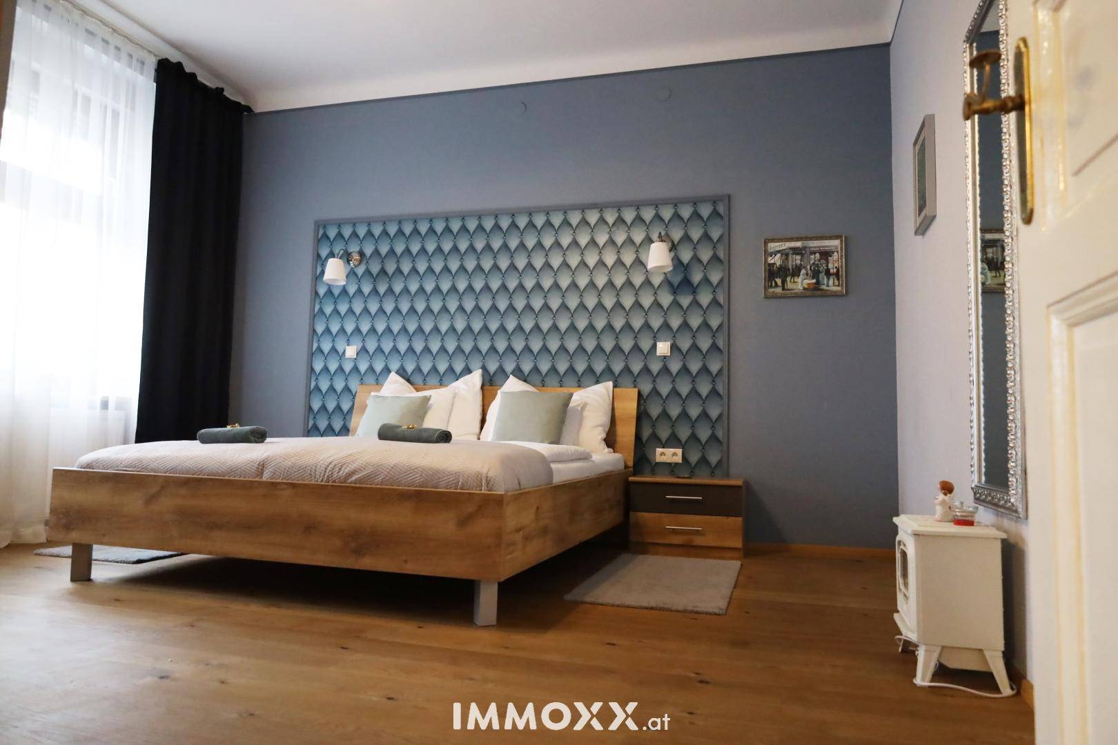 Geräumiges Schlafzimmer mit Holzbett, blauer Akzentwand und Parkettboden.