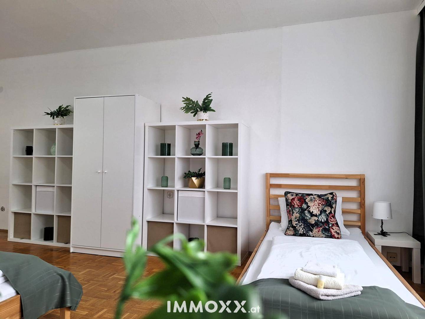 Schlafzimmer mit Einzelbett, Holzrahmen, weißem Kleiderschrank und Regalen.