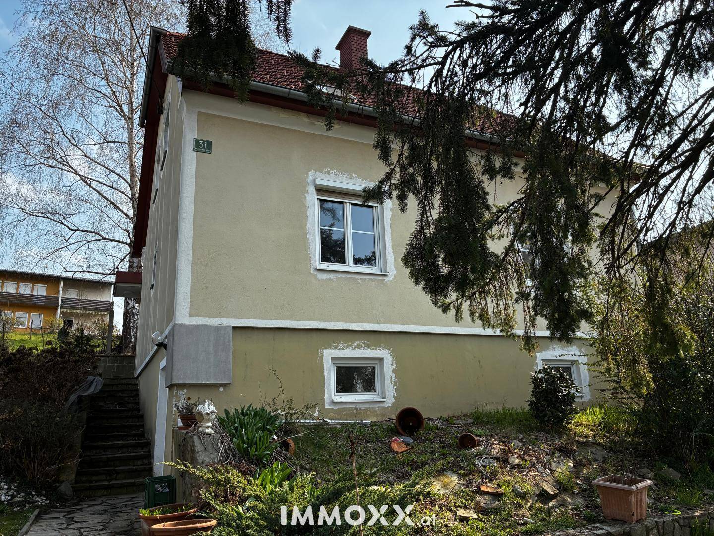 Fassade eines älteren Hauses mit mehreren Fenstern und einem kleinen Vorgarten.
