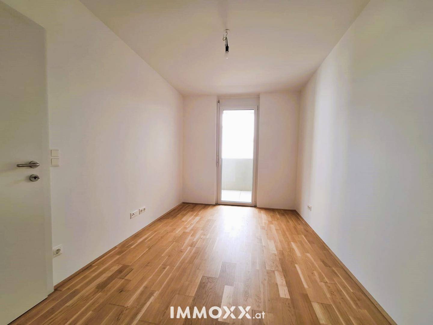 Helles Schlafzimmer mit Holzboden und Zugang zu einem kleinen Balkon, unmöbliert.