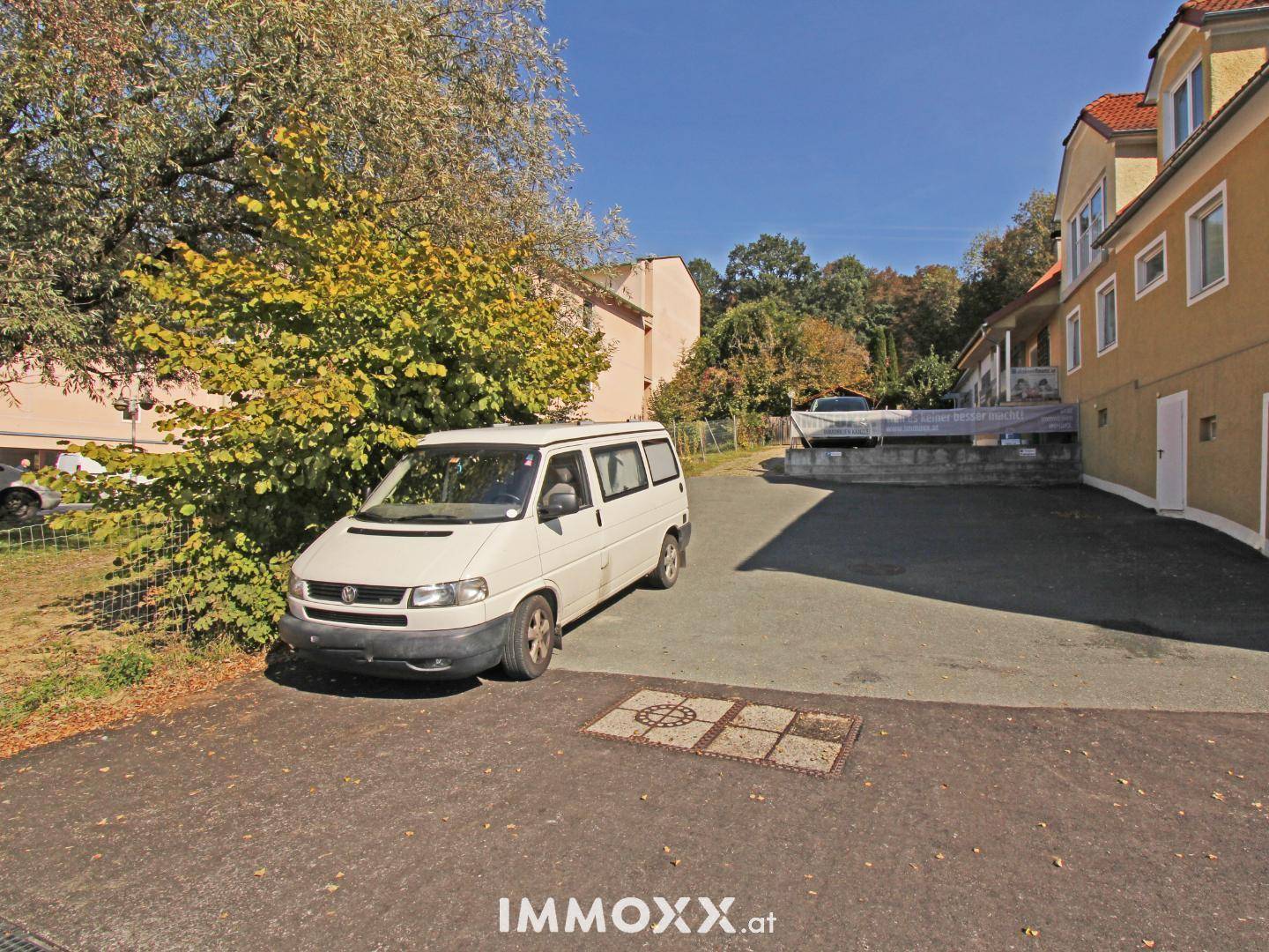 Außenbereich mit gepflastertem Parkplatz, einem geparkten Van und Bäumen.