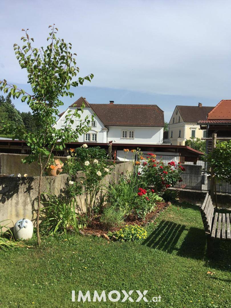 Blühender Garten mit Rasenfläche, Blumenbeeten und einem Sitzbereich im Freien.