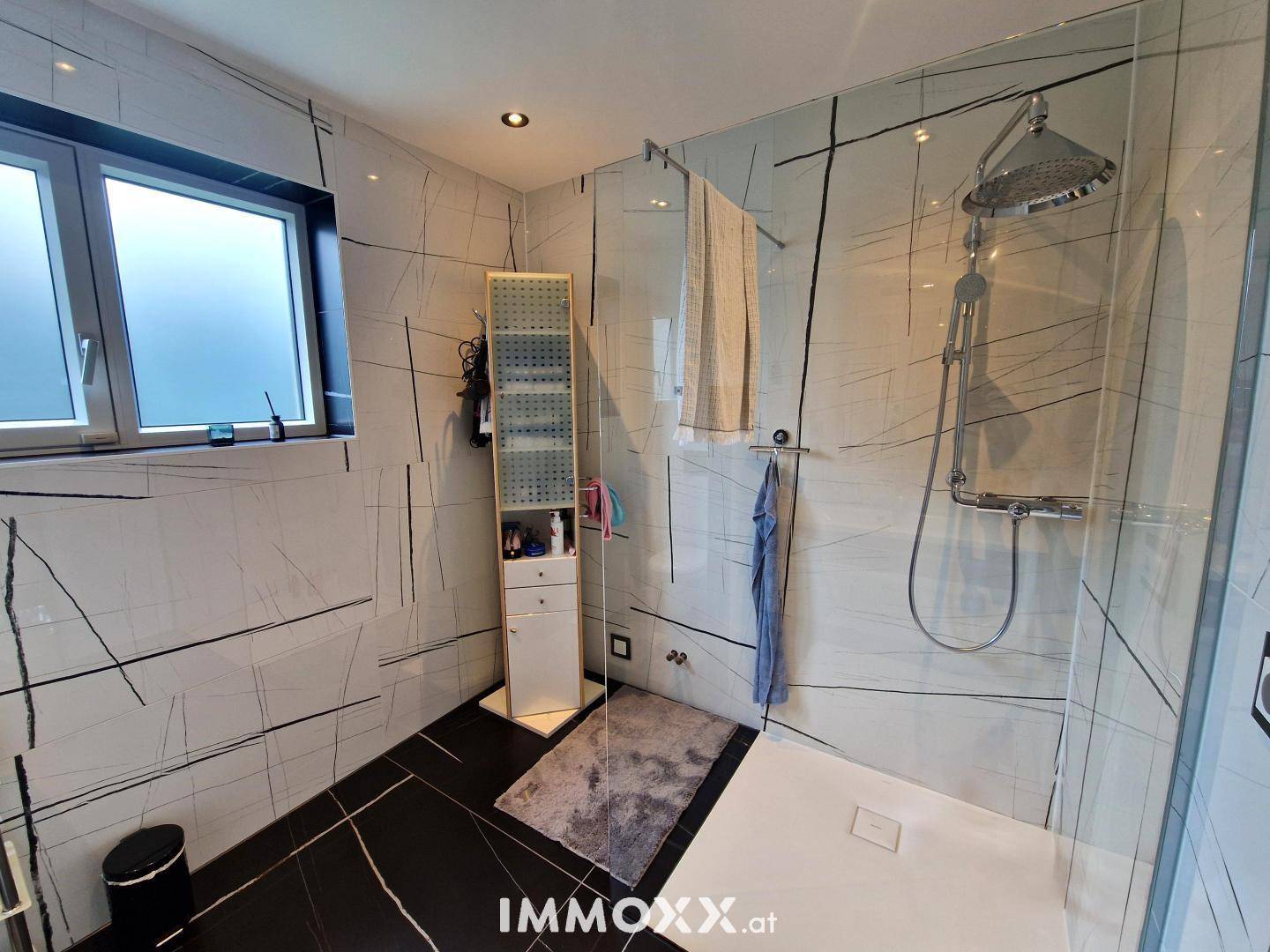 Modernes Badezimmer mit großformatigen Fliesen, begehbarer Dusche und Regenduschkopf.