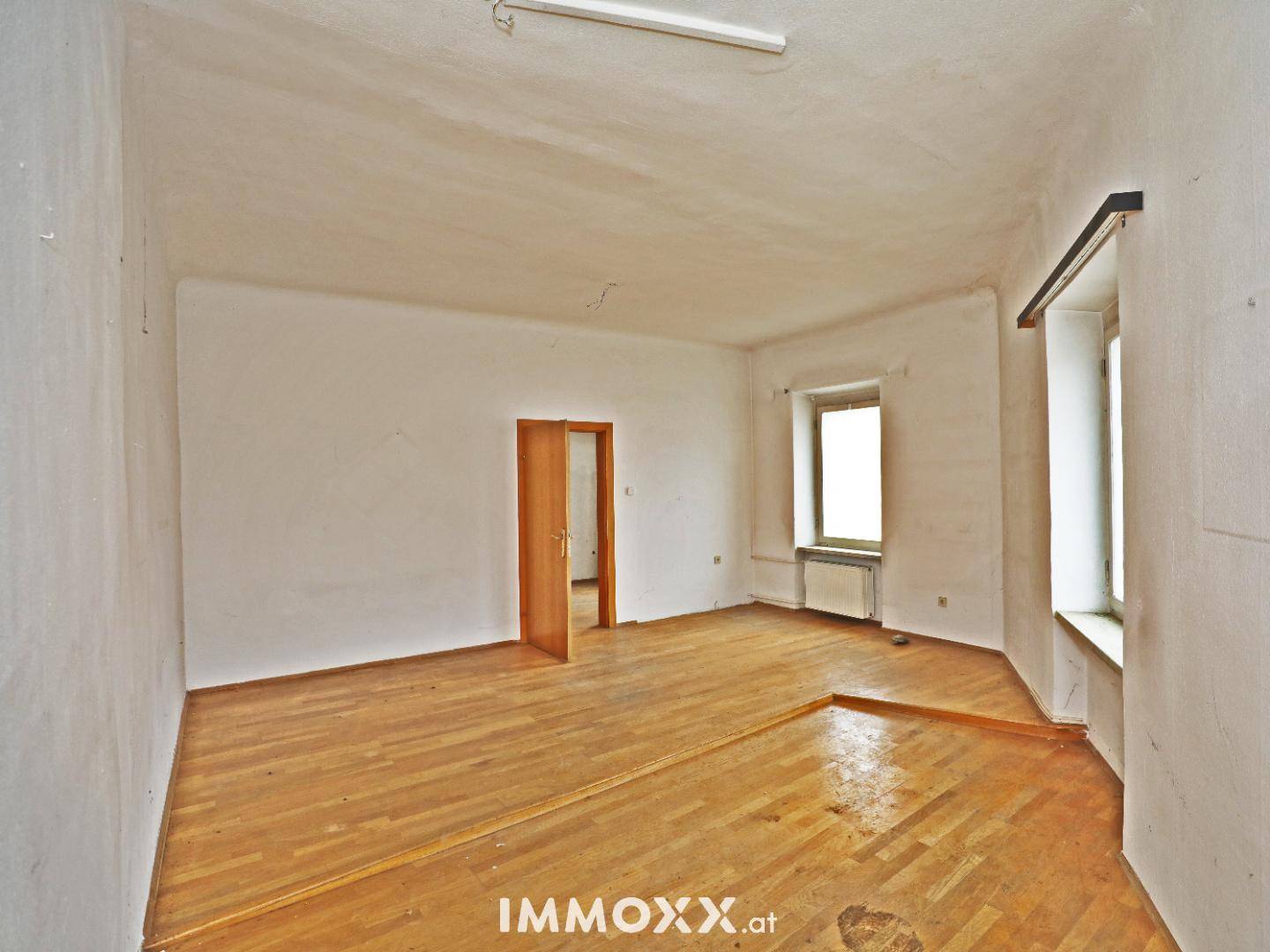 Geräumiger, leerer Raum mit Parkettboden und zwei Fenstern, bereit zur Renovierung.