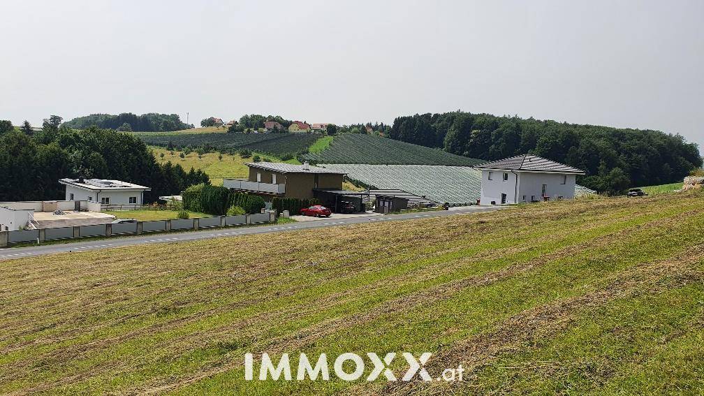 Weitläufige ländliche Landschaft mit grünen Hügeln, Feldern und vereinzelten Häusern unter klarem Himmel.
