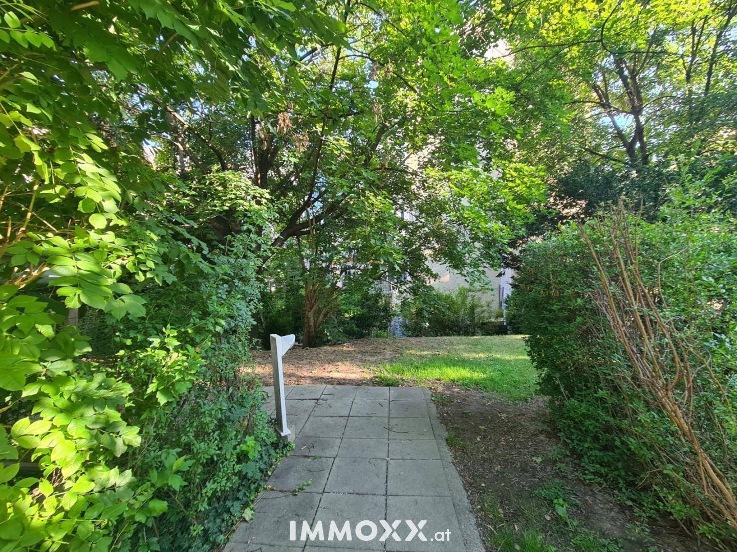 Gepflasterter Gartenweg führt durch üppiges Grün zu einem offenen Rasenbereich.