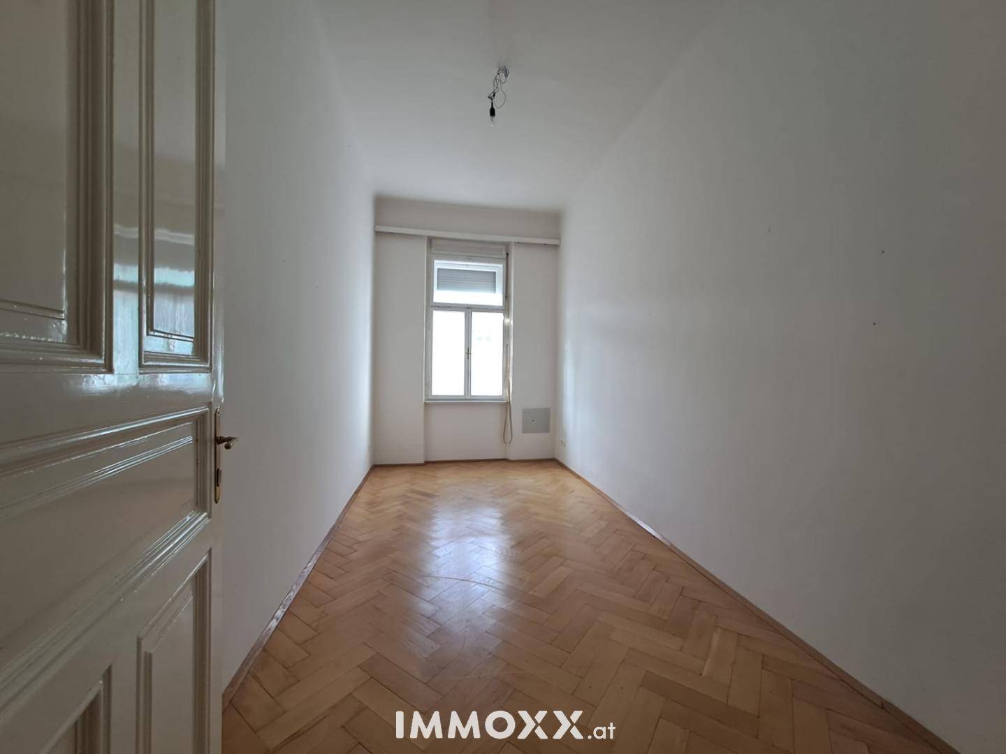 Schmaler, heller Raum mit Fischgrätparkettboden und einem Fenster, geeignet als Schlaf- oder Arbeitszimmer.