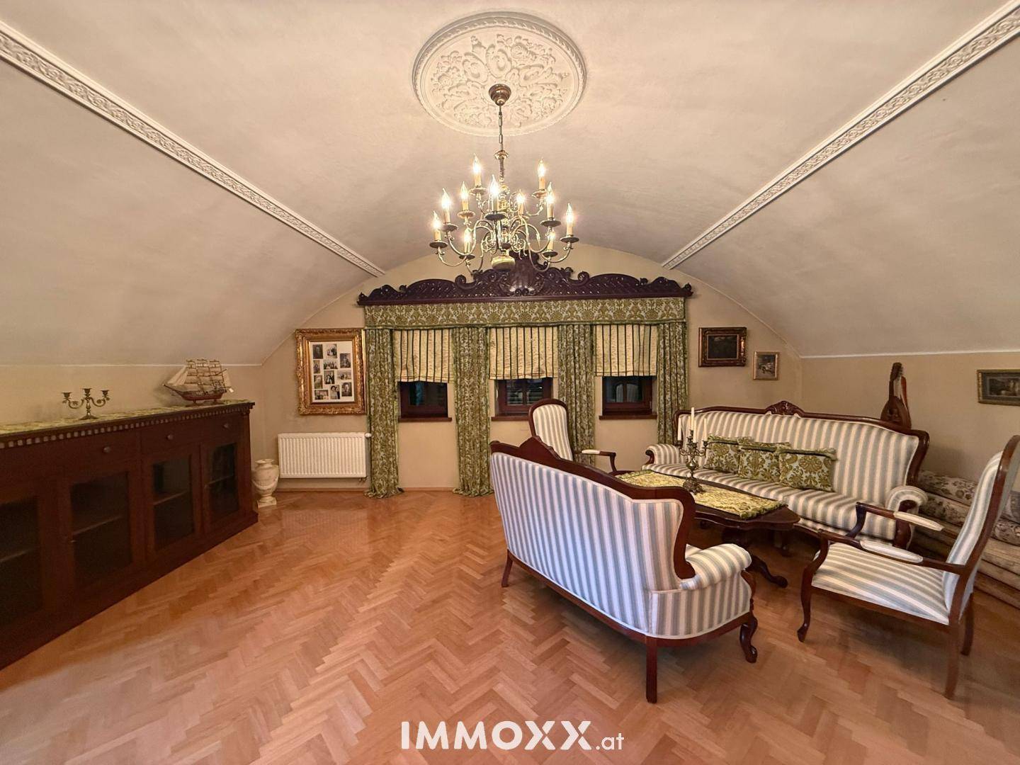 Gemütliches Wohnzimmer mit Dachschrägen, Fischgrätparkett, traditionellen Sofas und einem opulenten Kronleuchter.