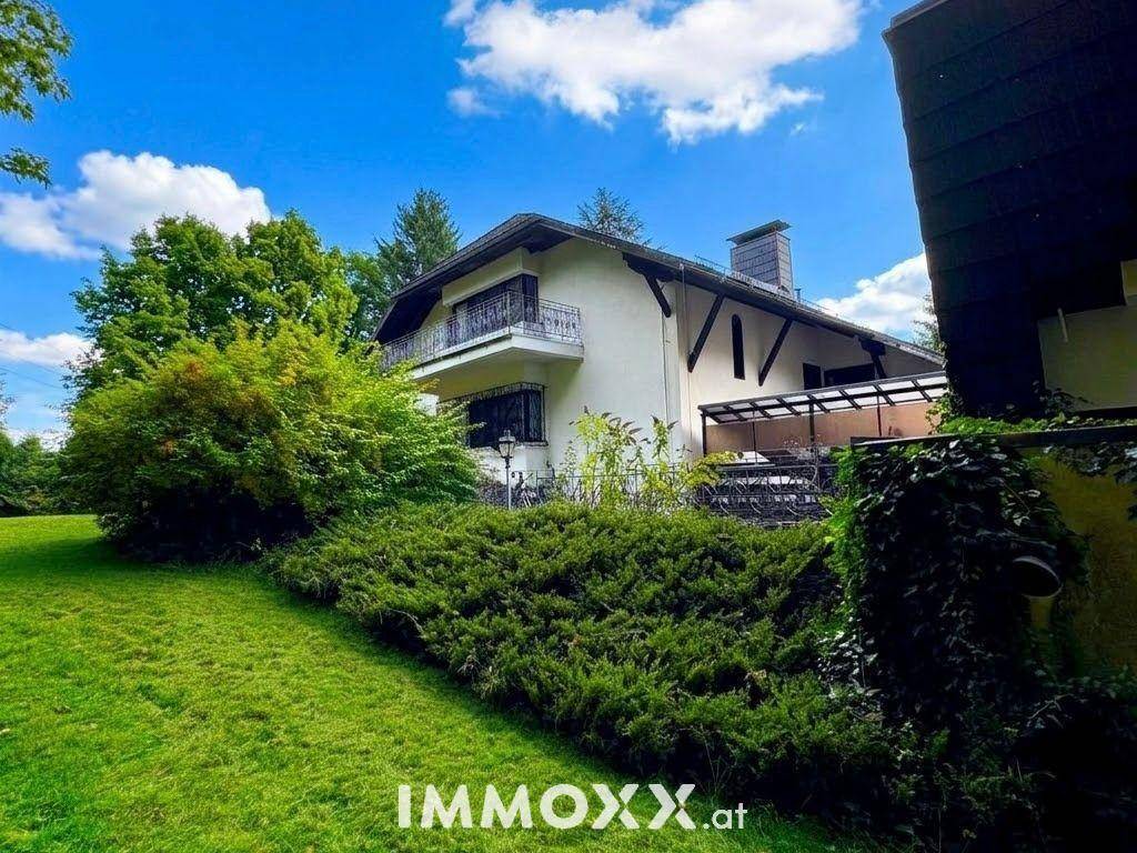 Großzügiger Gartenbereich mit Rasenfläche und einer überdachten Terrasse am Haus unter blauem Himmel.