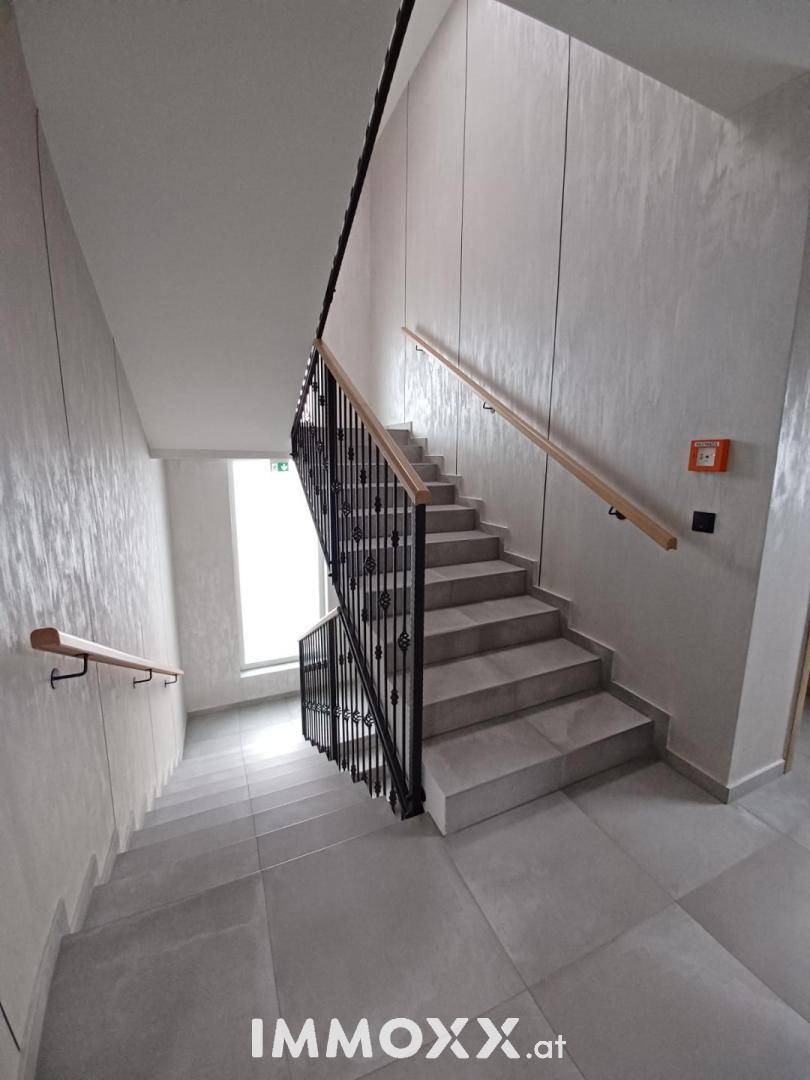 Treppenhaus mit modernen Fliesen, Holzhandläufen und schmiedeeisernem Geländer.