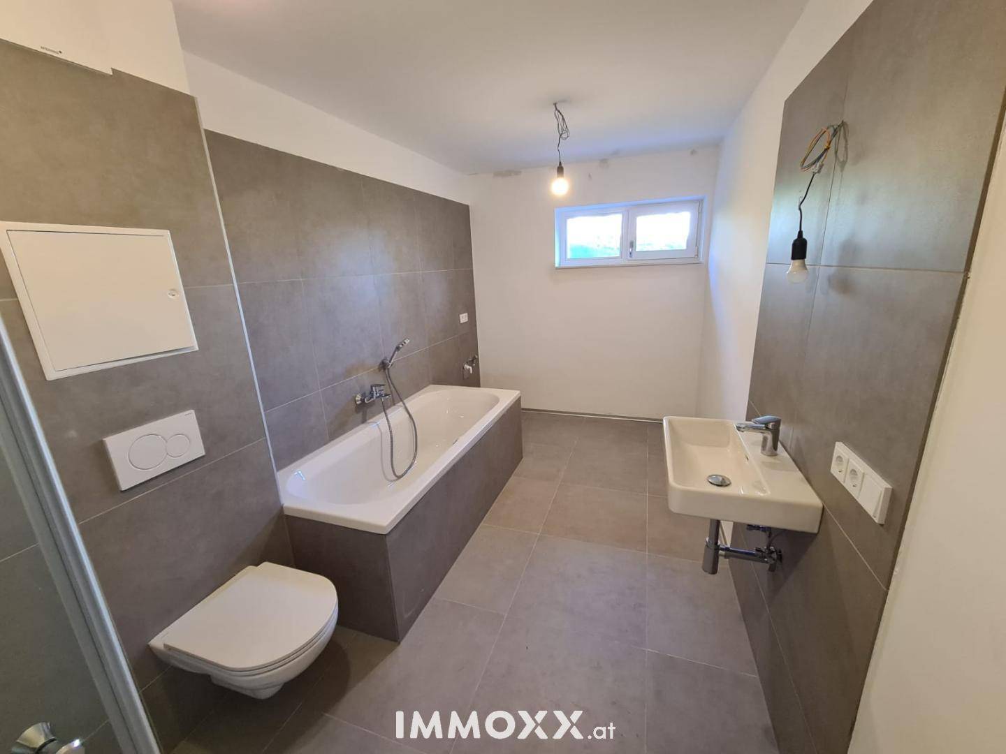Geräumiges Badezimmer mit Badewanne, WC, Waschbecken und Fenster für Belüftung.