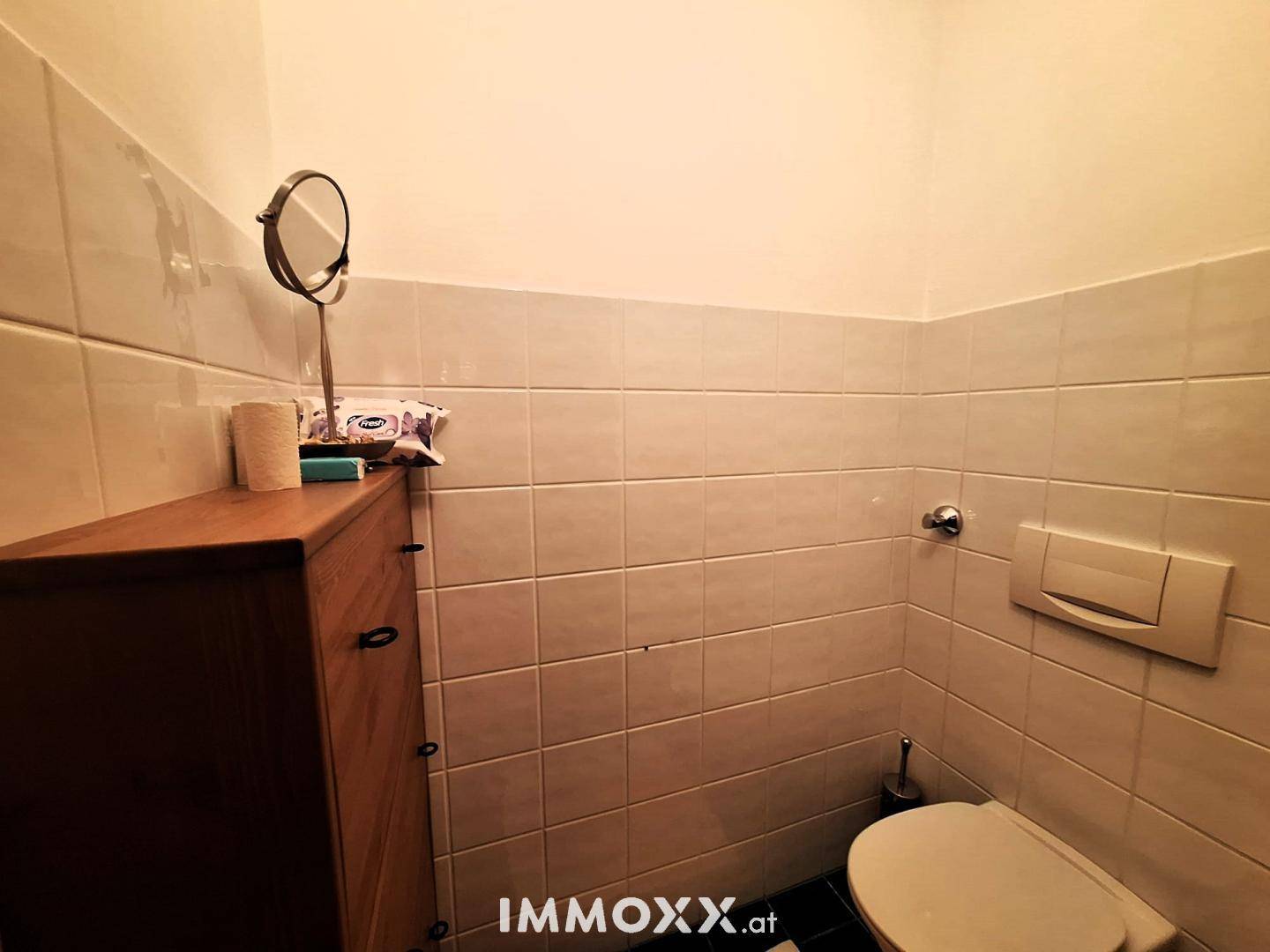 Separates WC mit hellen Wandfliesen und einer kleinen Ablagefläche.