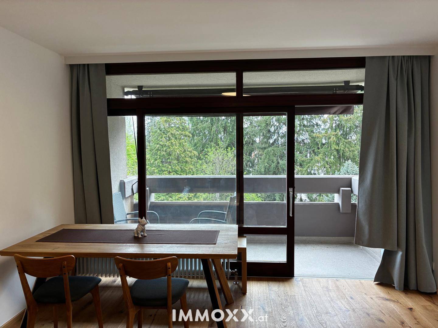 Heller Essbereich mit Holztisch und großem Fenster, das Zugang zu einem Balkon bietet.