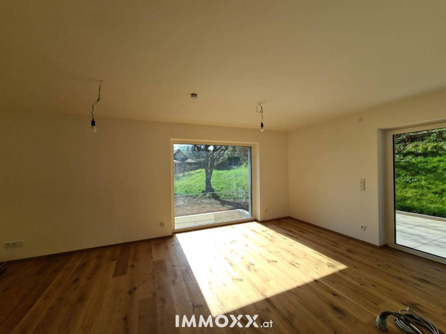 Geräumiger Wohnbereich mit hellem Holzfußboden und großen Fenstern für viel Tageslicht.