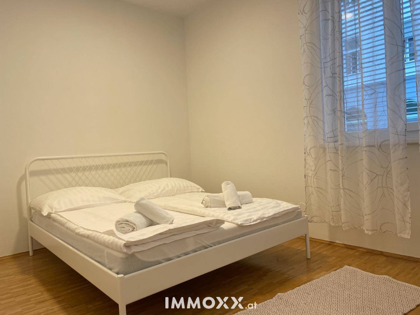 Gemütliches Schlafzimmer mit Doppelbett, Holzboden und Vorhängen am Fenster.