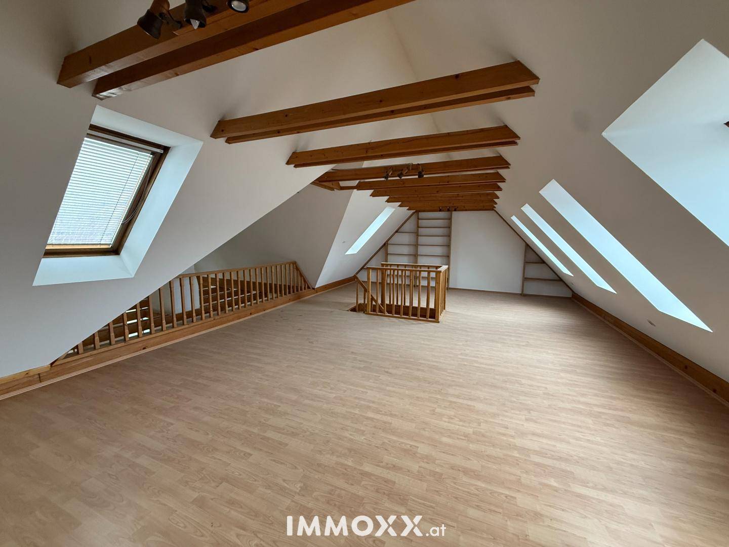 Heller Dachbodenraum mit Holzbalken, Dachschrägen und einem Geländer, bereit zum Ausbau.