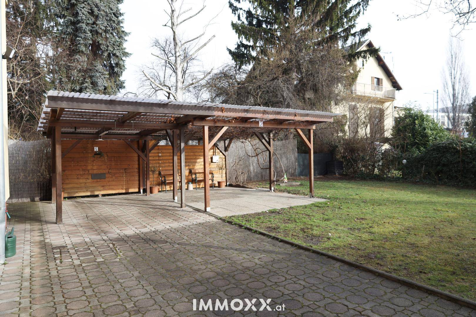 Großer Garten mit Rasenfläche und überdachtem Carport für Fahrzeuge.
