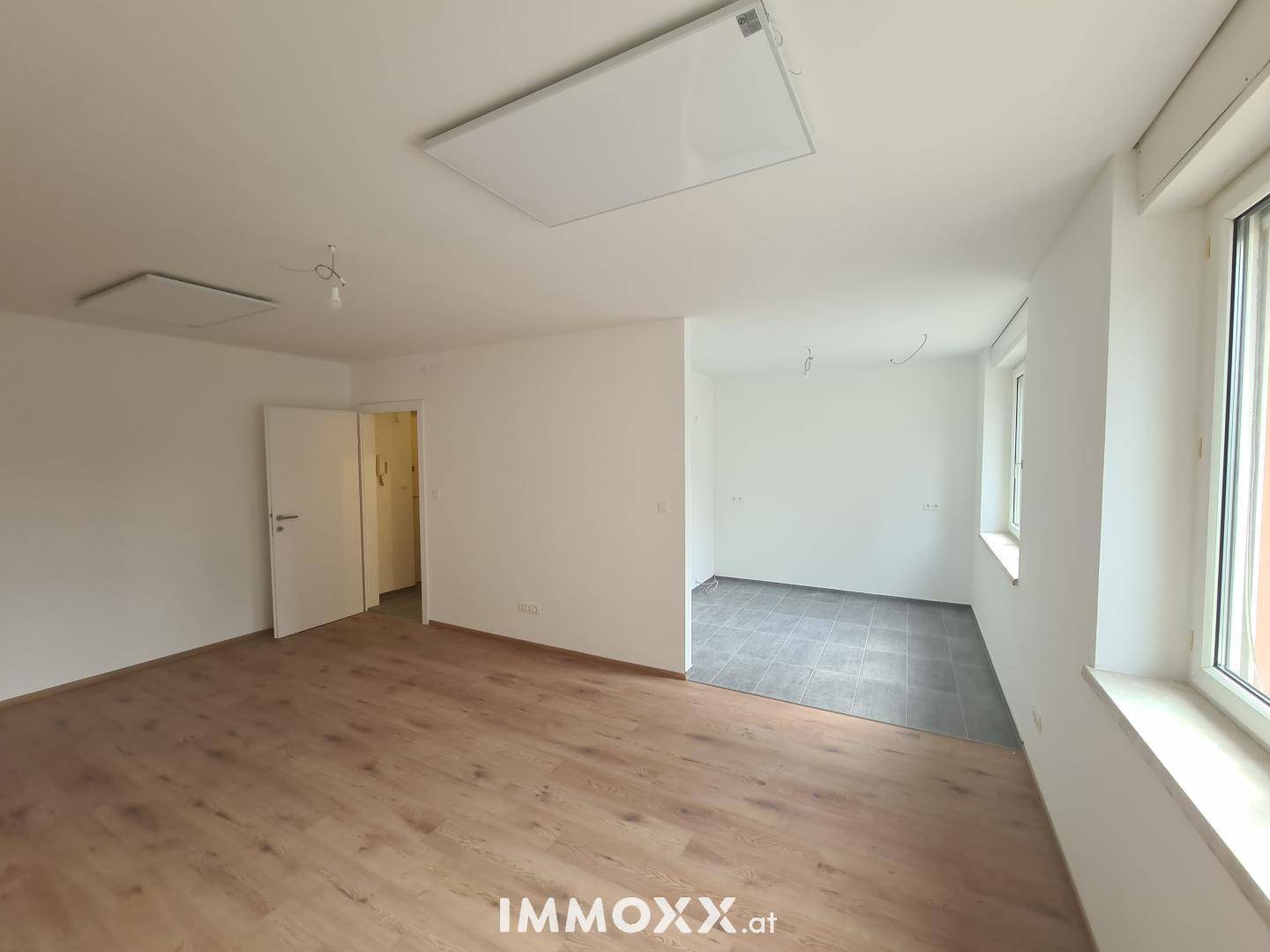 Heller Wohnbereich mit Laminatboden und angrenzendem gefliesten Bereich, ideal für offenes Wohnen.