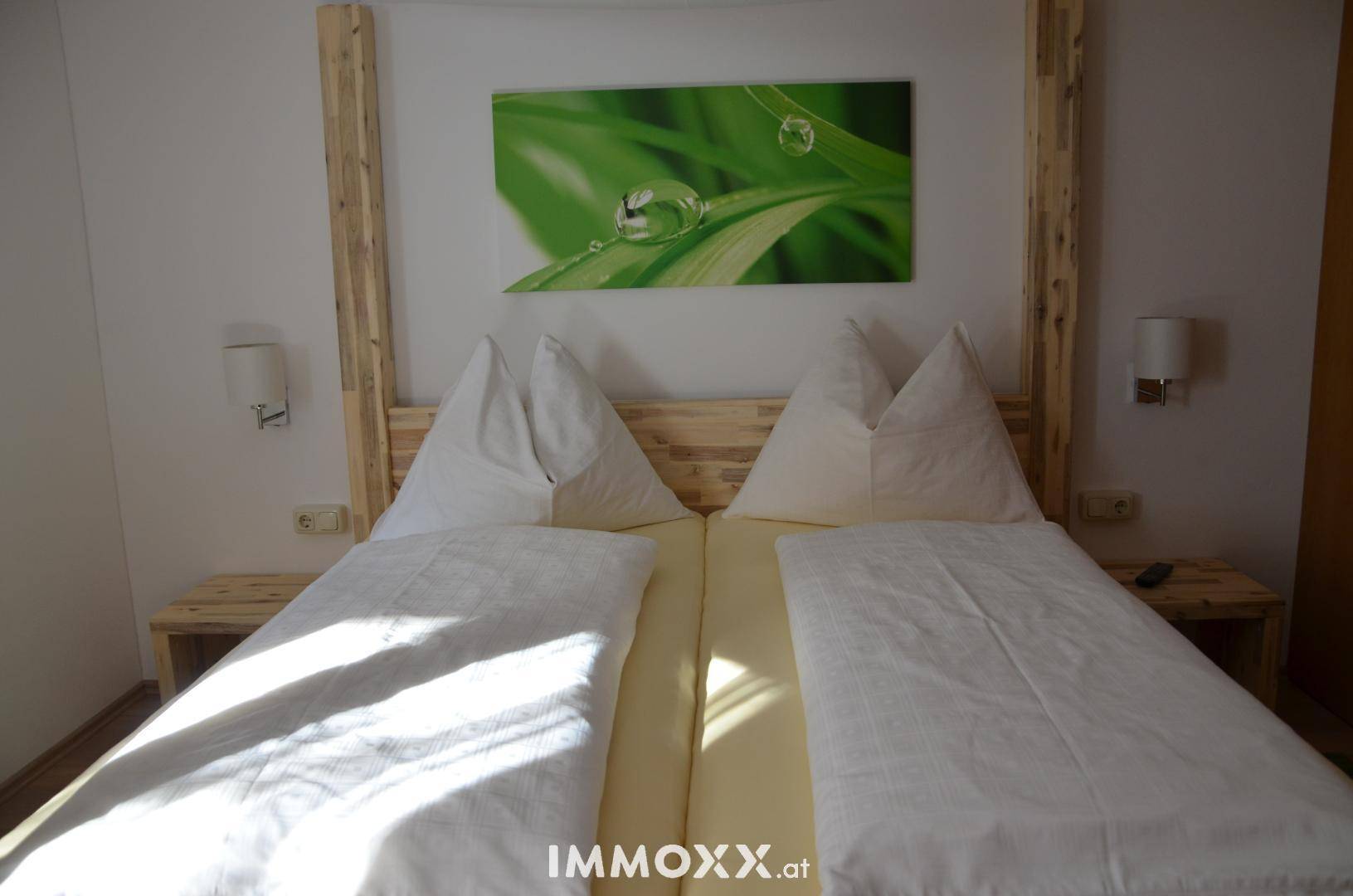 Nahaufnahme eines Himmelbettes aus hellem Holz mit Nachttischen und Wandlampen in einem gemütlichen Schlafzimmer.