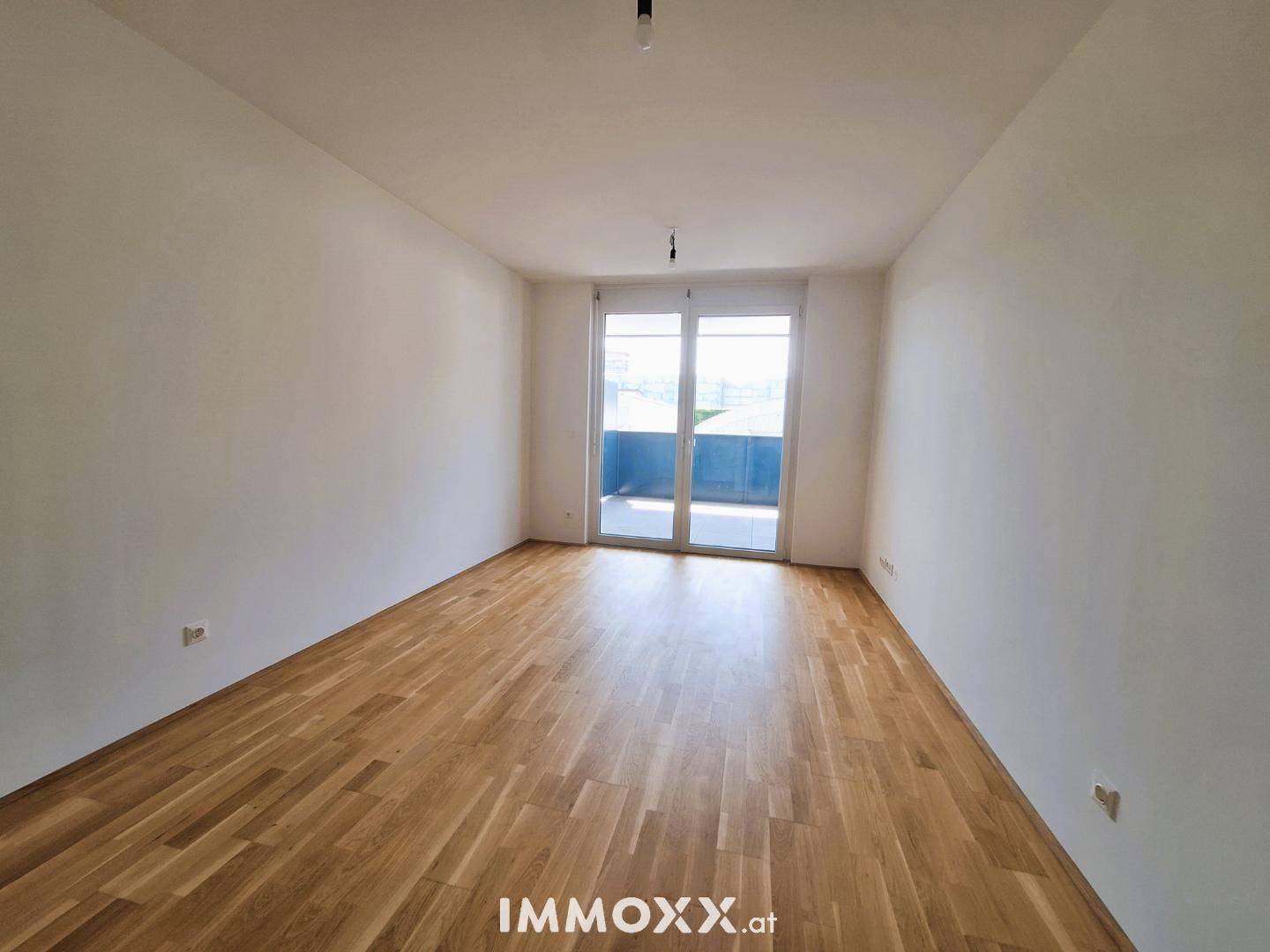 Geräumiger, heller Raum mit Parkettboden und Zugang zu einem Balkon.