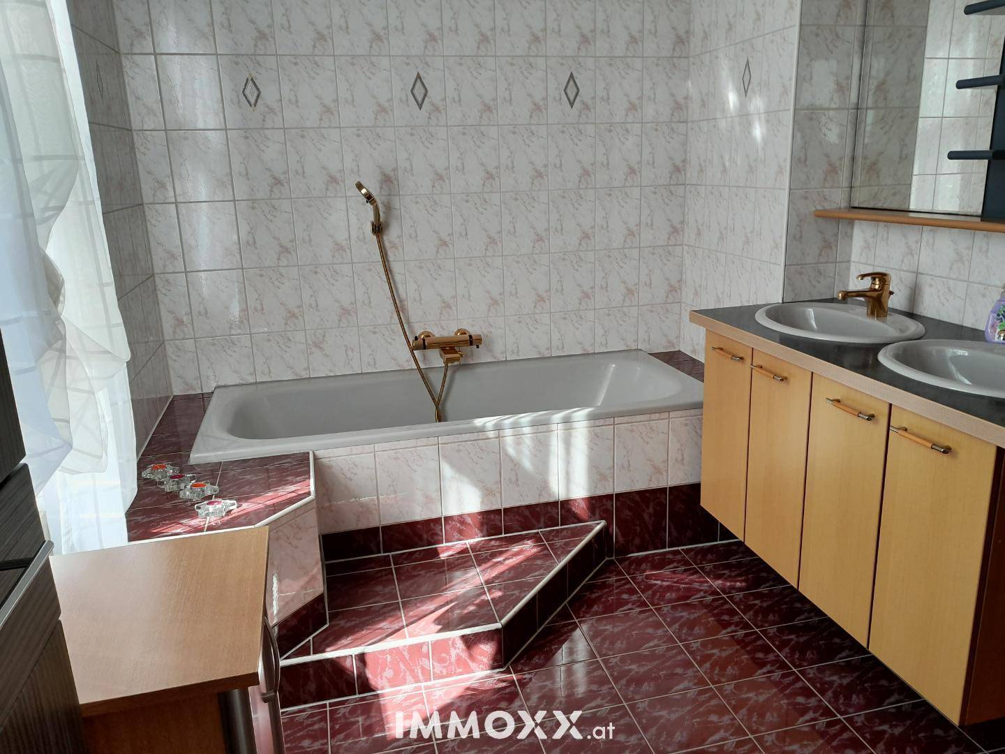 Badezimmer mit Badewanne, Doppelwaschbecken und Fliesen in warmen Farbtönen.