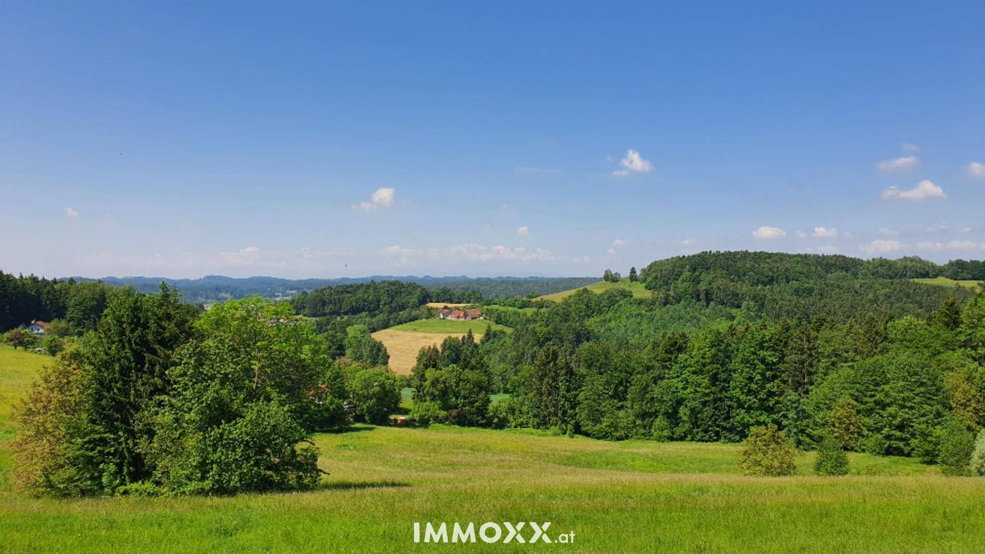 Idyllische ländliche Umgebung mit weiten Wiesen, Bäumen und sanften Hügeln.